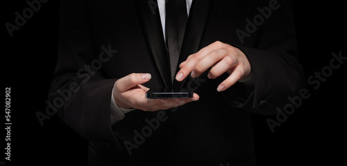 Business person in black siut hand with mobile phone against black background photo