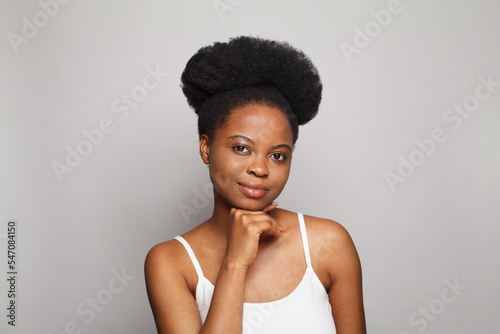 Beauty portrait of young woman with shiny skin looking at camera and touching her chin with her hand.