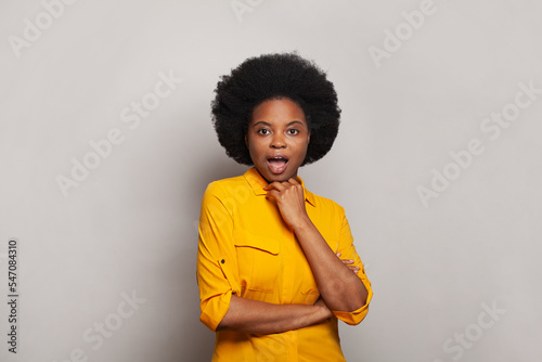 Happy excited young woman brunette in yellow shirt standing against white studio wall background