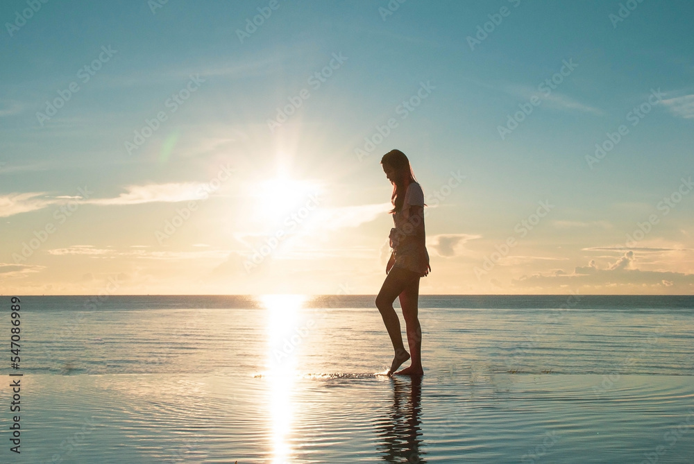 Asia woman walking alone the sea view infinity pool in sunrise, morning time