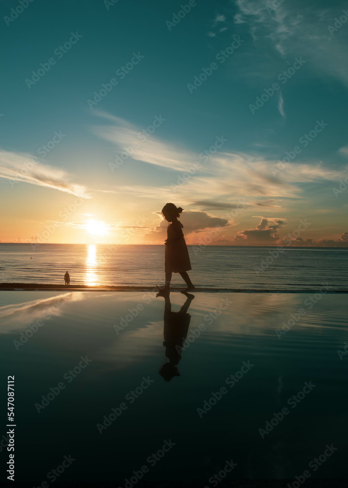 A girl walking along the infinity pool sea view in the sunset time.