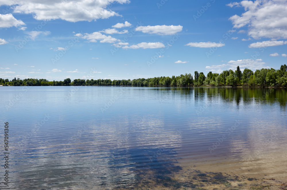 Beautiful river landscape. Lake surface on a sunny perfect day. The surface of the water against the background of trees and a blue sky. Blurred image, selective focus