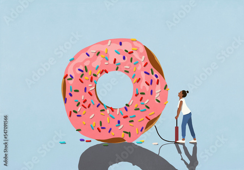 Woman with bicycle pump inflating large donut with sprinkles
 photo