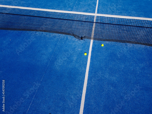 Overhead aerial view of two balls near the net of a blue paddle tennis court © Vic
