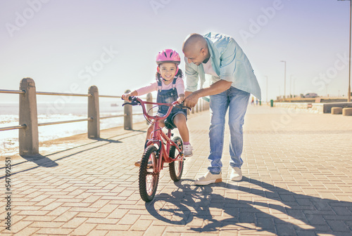 Murais de parede Father, child and bicycle with a girl learning to ride a bike on promenade by sea for fun, bonding and quality time on summer vacation
