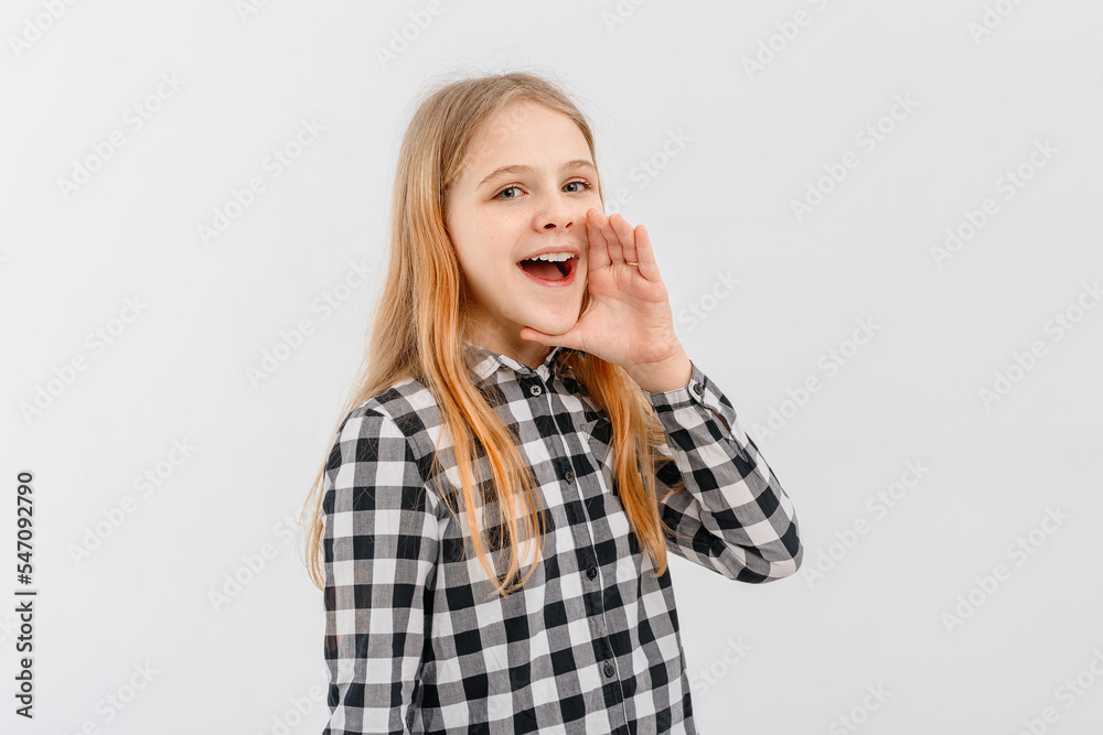 Attractive teen girl holding palm near wide open mouth is announcing, telling a secret, shouting or yelling, standing in casual plaid shirt over white background. Communication and promo concept Attractive teen girl holding palm near wide open mouth is announcing, telling a secret, shouting or yelling, standing in casual plaid shirt over white background. Communication and promo concept