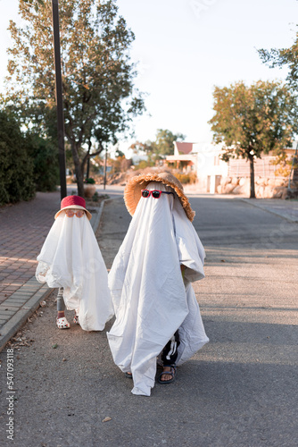 Trendy sheet ghosts costumes on little kids standing on a suburbs street. Happy halloween holiday 