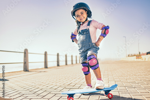 Summer, happy and little girl portrait with skateboard for holiday in Los Angeles with sky mockup. Vacation, sidewalk and cute black child with helmet ready to skate for wellness, health and fun.