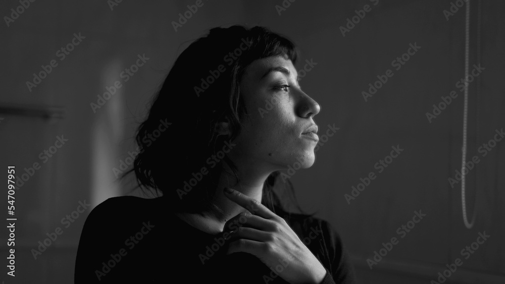 Contemplative woman standing by mirror looking out in monochrome black and white Contemplative woman standing by mirror looking out in monochrome black and white