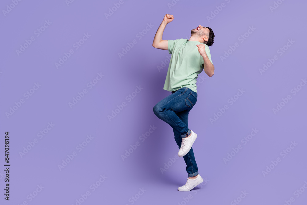 Full length photo of overjoyed ecstatic champion guy with brunet hairdo dressed t-shirt raise fists up isolated on purple color background Full length photo of overjoyed ecstatic champion guy with brunet hairdo dressed t-shirt raise fists up isolated on purple color background
