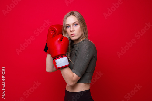 Young athletic female boxer posing for the camera on a red background