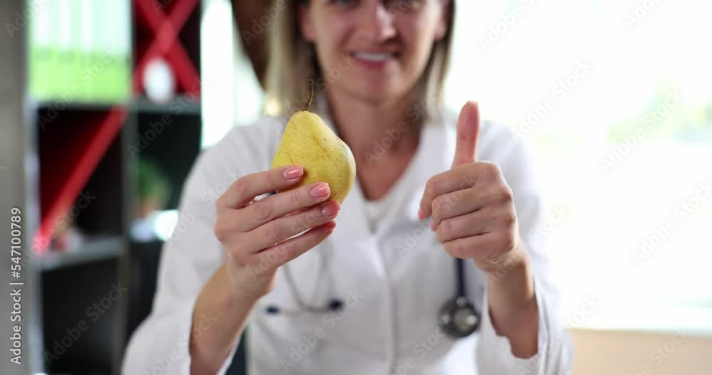 Smiling happy female doctor holding yellow pear and showing thumb up Smiling happy female doctor holding yellow pear and showing thumb up