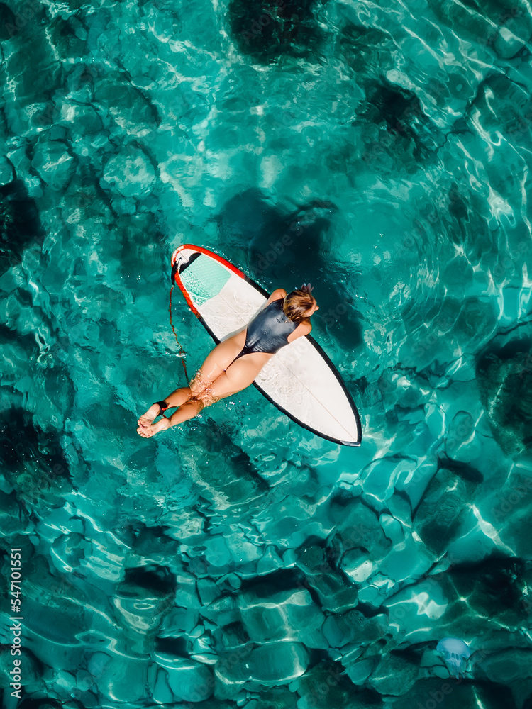 Attractive woman floating on surfboard in tropical ocean. Aerial top view