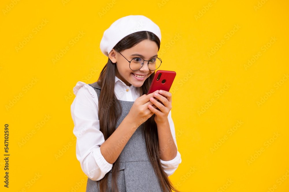 Surprised teenager child holding cellphone. Close-up portrait of cute teen girl using mobile phone, cell web app, isolated over yellow background. Surprised teenager child holding cellphone. Close-up portrait of cute teen girl using mobile phone, cell web app, isolated over yellow background.