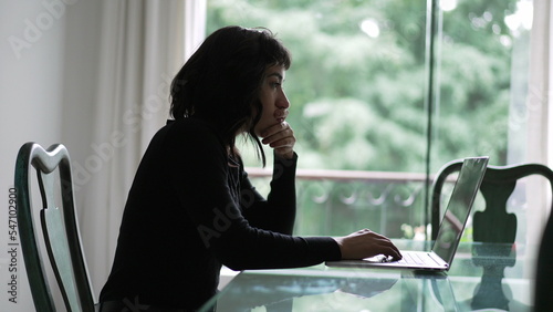 A pensive hispanic girl in front of laptop thinking. Thoughtful South American woman studying using computer2 photo