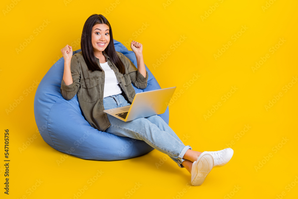 Full body size photo of young developer laptop japanese woman sit comfort beanbag celebrate first project done isolated on yellow color background