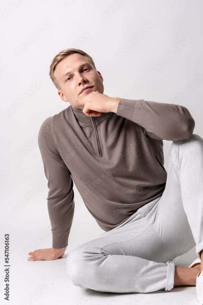 Caucasian blond model with a brown sweater on a white background, sitting on the floor with a seductive look Caucasian blond model with a brown sweater on a white background, sitting on the floor with a seductive look