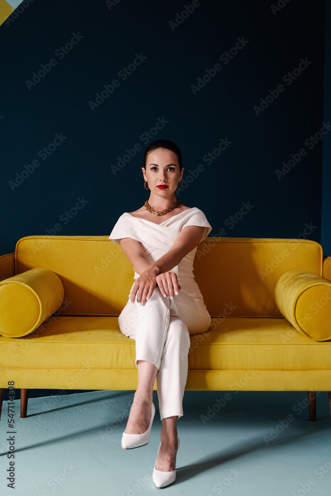 Naklejka premium a girl in a white jumpsuit sits beautifully on a yellow sofa