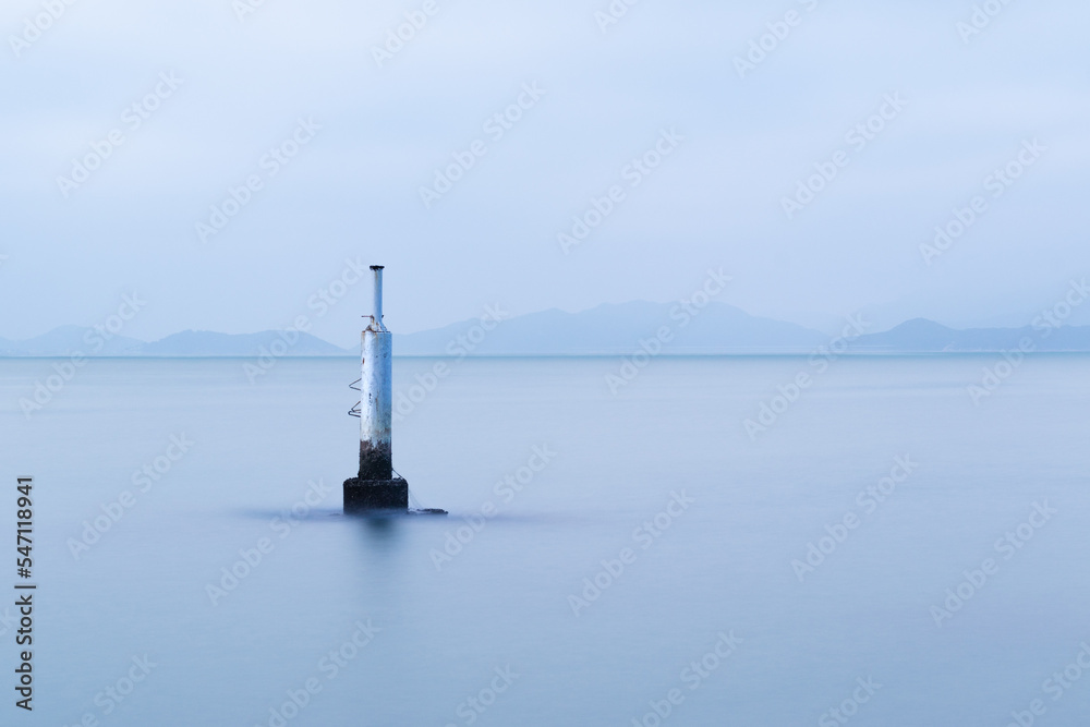 Concrete post in the sea probably for mooring or navigation.  Long exposure gives the sea a smooth surface.
