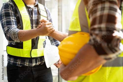 construction worker wearing a protective helmet and vest is holding his colleague's hand while working.