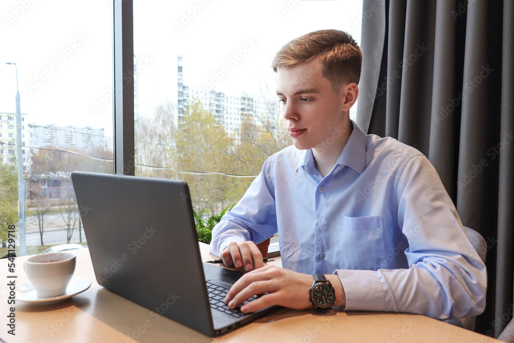 A young man works at a laptop at a table in the room. 