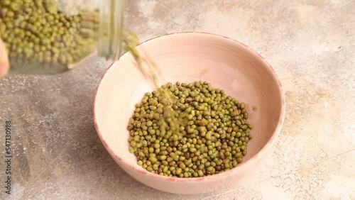 mung beans pour into a ceramic bowl on a brown concrete background, side view, close up