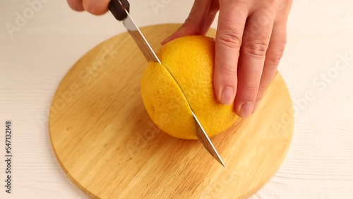 Male hand cuts fresh orange with a knife on wooden kitchen board. Side view, close up.