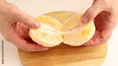 Male hand divide into slices peeled fresh orange with hands on wooden kitchen board. Side view, close up.