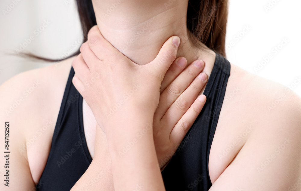 A woman suffering from esophagitis is touching her wrinkled neck.