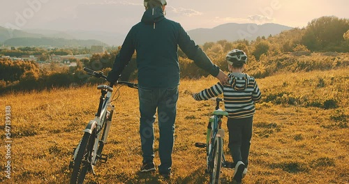 Title: Father teaching son to ride bicycle. Happy cute boy in helmet learn to riding a bike in park on green meadow in summer day at sunset time. Family weekend. 4K video Slow

