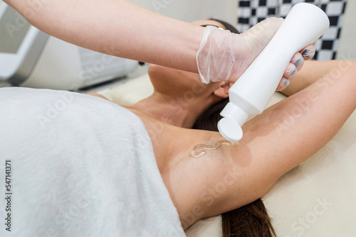 The cosmetologist applies a special transparent gel to the skin of the armpit.
