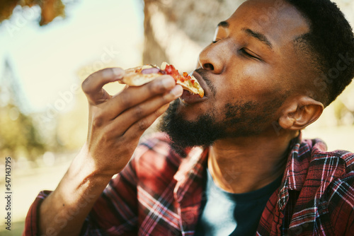 Fotografiet Fast food, hungry and black man eating pizza for delicious and yummy lunch break in park