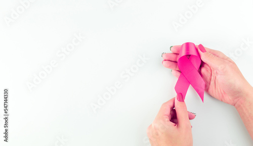 Pink ribbon banner. Woman hands holding health care symbol pink ribbon on white background. Breast cancer support with copy space.