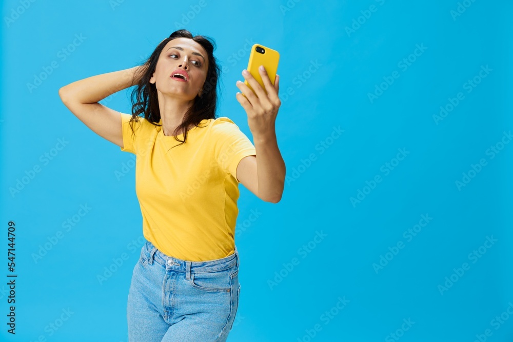 Woman with a phone in her hands with a yellow case on a blue background in a yellow T-shirt, emotions signals gestures, online lifestyle concept, shopping, communication, learning, business online Woman with a phone in her hands with a yellow case on a blue background in a yellow T-shirt, emotions signals gestures, online lifestyle concept, shopping, communication, learning, business online