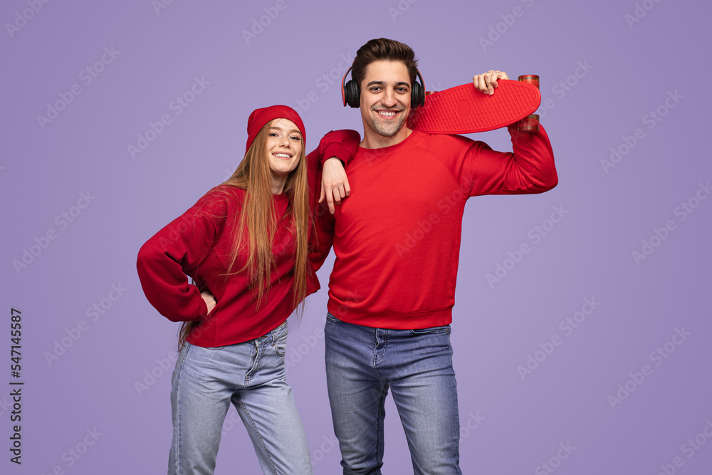 Obraz premium Cool young couple with skateboard smiling at camera in violet studio