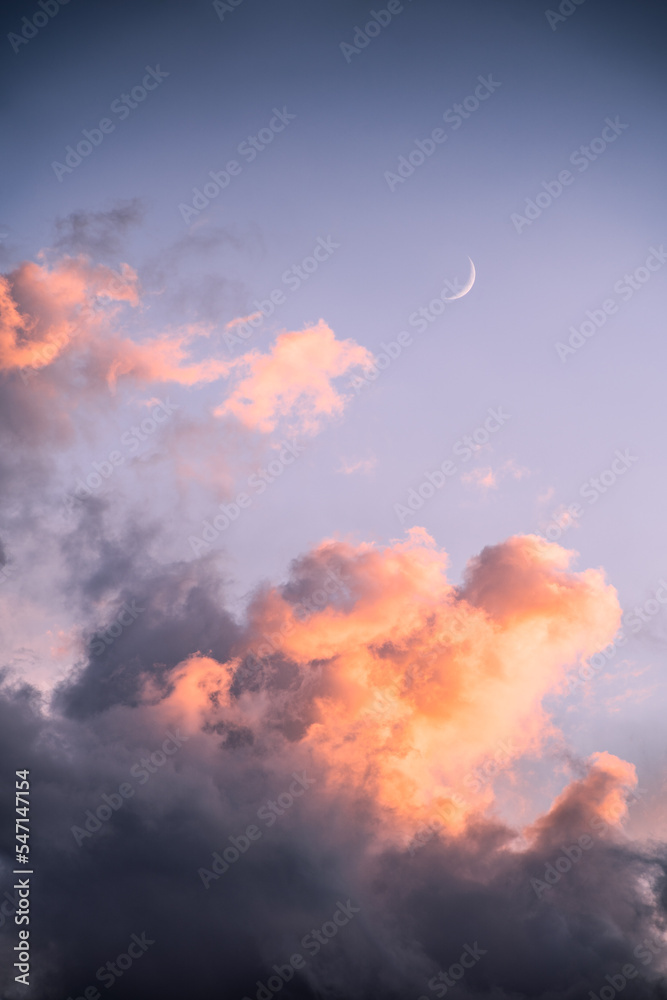 The Moon appears behind some colorful clouds at sunset after a summer storm