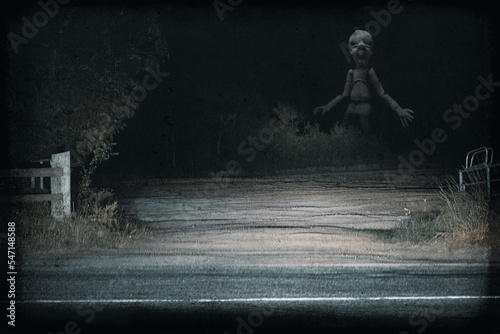 A giant horror doll. Lit up by car headlights in the countryside at night. With a spooky found footage edit.