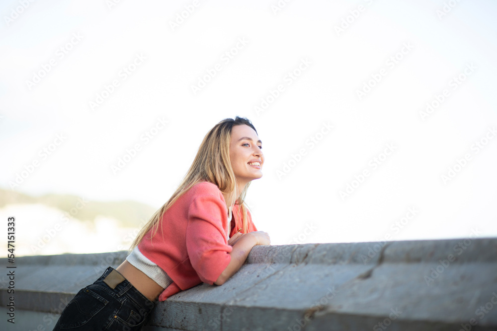 smiling young blond woman leaning outdoors and looking away