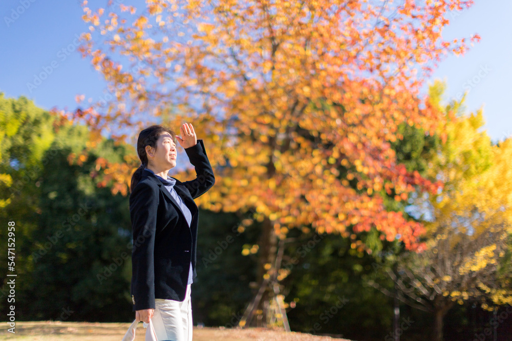 秋の公園で散歩している中年女性と綺麗な紅葉の風景