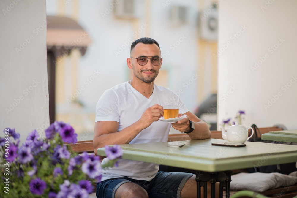 a cute man is drinking tea in a cafe on the street, a sexy guy is having breakfast in a cafe