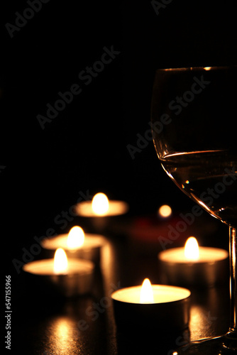 A glass of red wine and a candle on a black background.