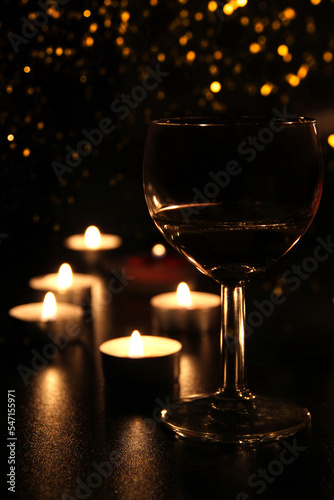 A glass of red wine and candles on a black background with light lights.