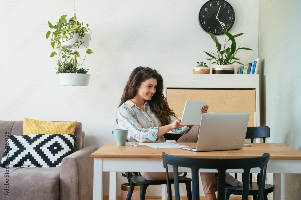 Smiling business woman reading report on her tablet while working at home office desk with a cup of coffee, laptop computer, paper and pen Smiling business woman reading report on her tablet while working at home office desk with a cup of coffee, laptop computer, paper and pen