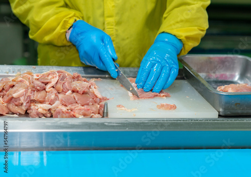 Hand of worker cut and trim chicken meat on cutting board.