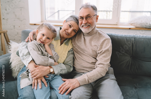 Grandparents embracing with granddaughter on sofa