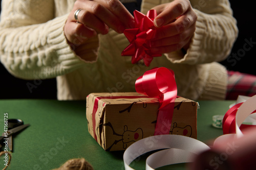 Woman decorates a Christmas gift with tied bow. Boxing Day. Packing presents for New Year or any other celebration event