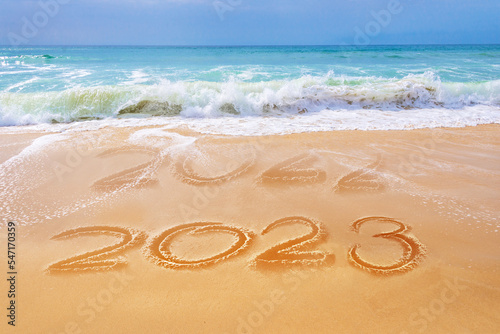 2023 written on the sand of a beach, ocean waves, travel new year greeting card