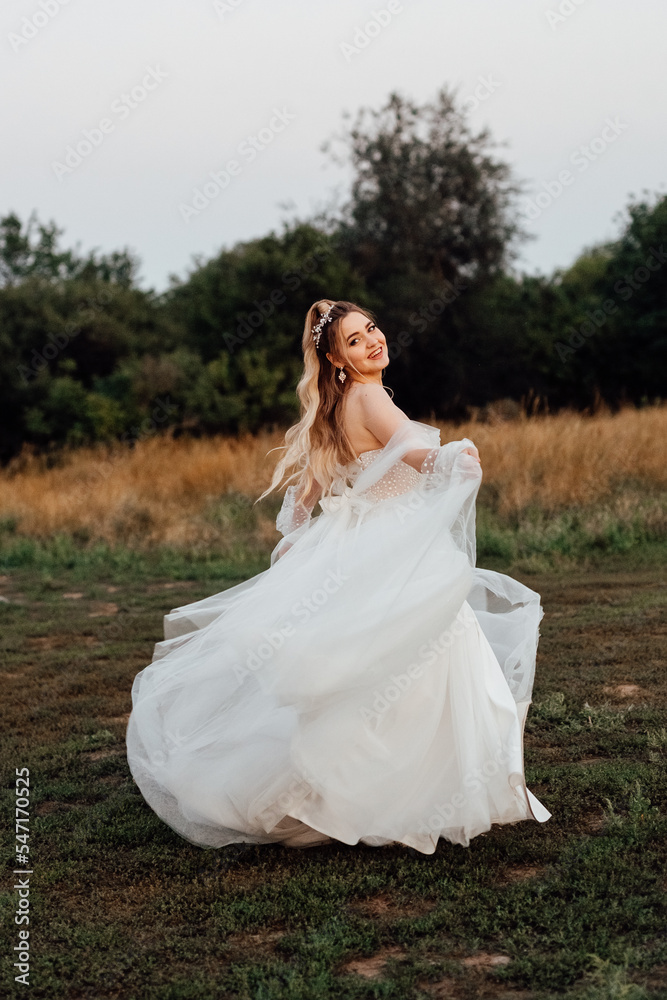 a cheerful, beautiful bride, laughing and looking around, runs across the field in a wedding dress