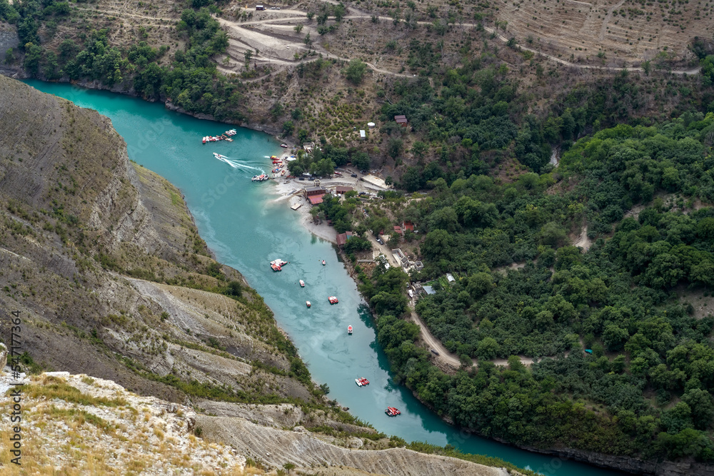 Turquoise river Sulak meandering through rocky forested landscape. Gorge of mountain river with village and boats