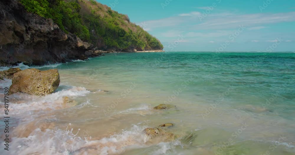 Turquoise ocean water spalshes blue waves rushing to the rocky shore Green Bowl Beach. Relaxing background of tropical paradise Island Bali Indonesia.